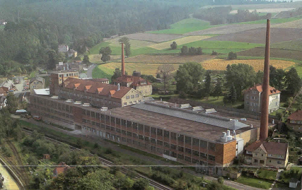 Luftaufnahme der Porzellanfabrik Arzberg mit langem Hallengebäude und Schornsteinen.
