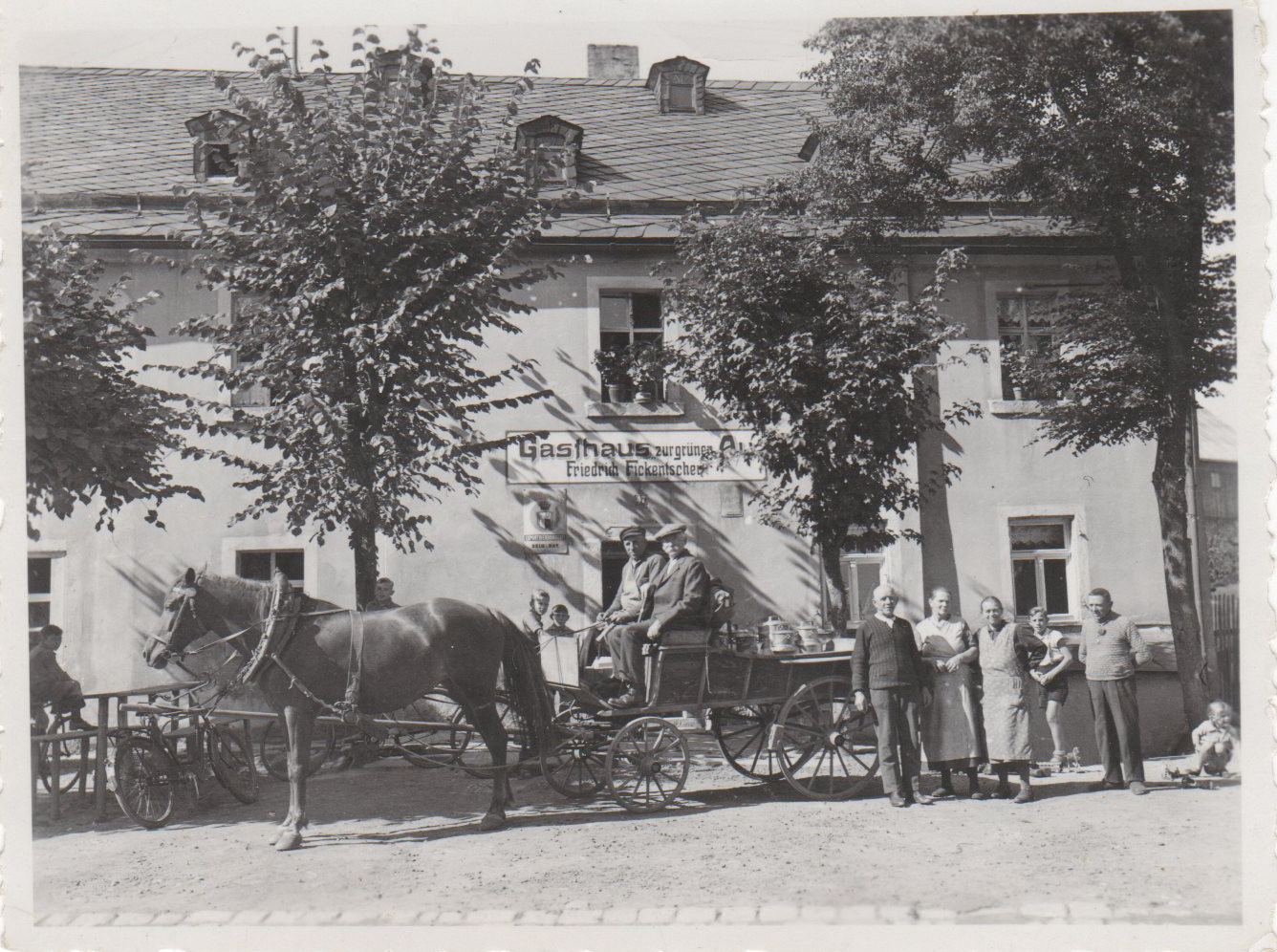 Historische Ansicht des Gasthauses Zur grünen Au mit Pferdegespann und Menschen vor dem Gebäude.