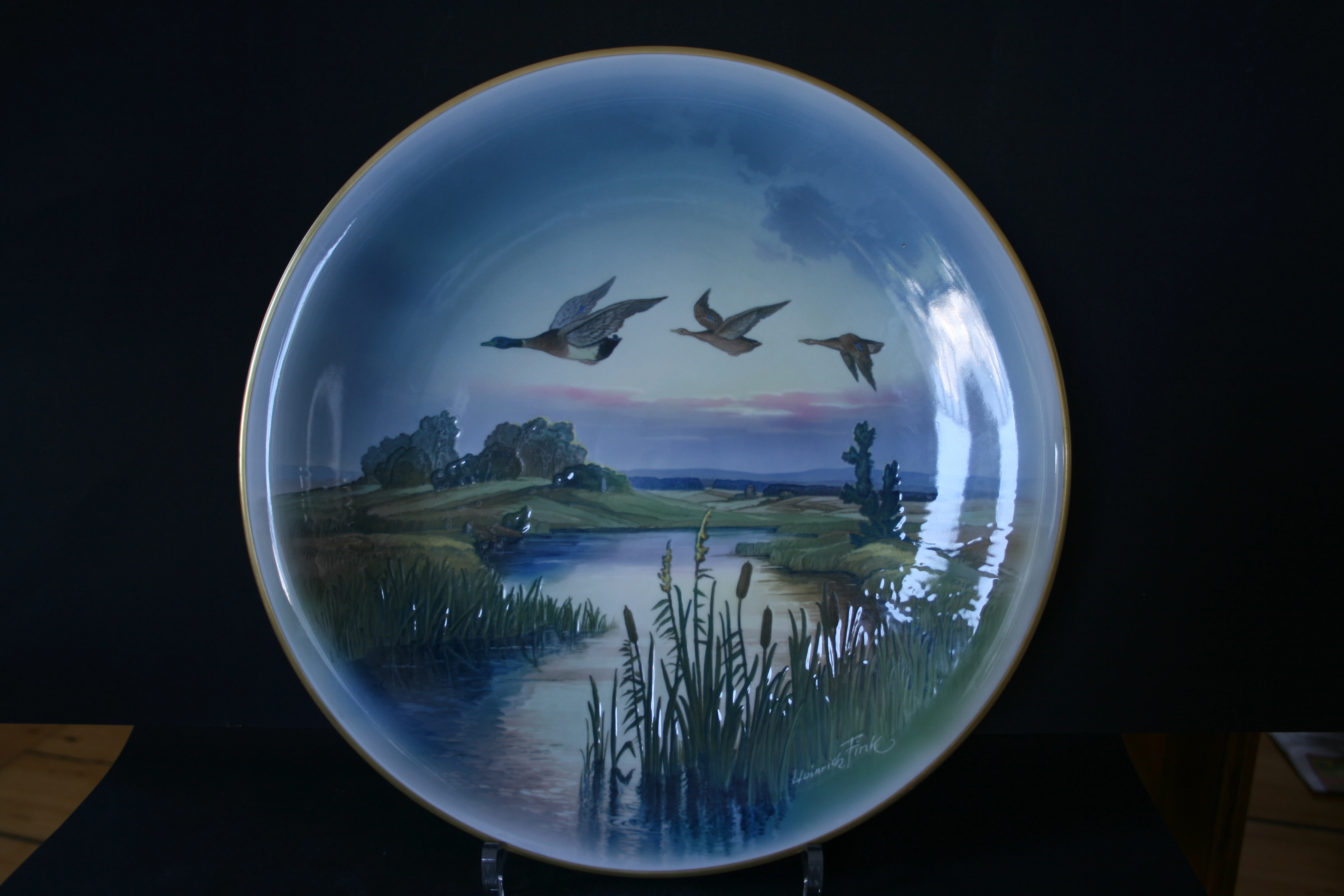 Vollständige Ansicht eines bemalten Wandtellers mit Enten im Flug über Schilf und Wasserlandschaft.