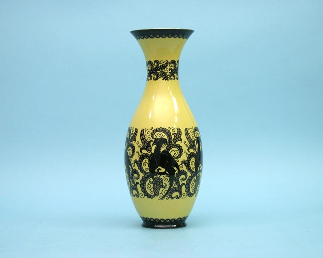Schlanke gelbe Porzellanvase mit schwarzem Ornament und ausgestellter Mündung vor blauem Hintergrund.