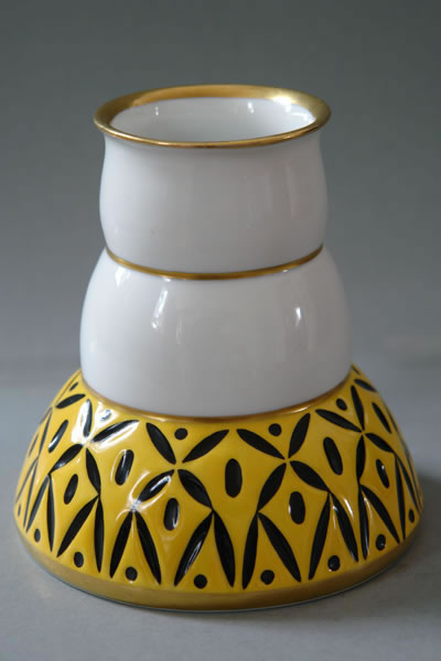 Kleine Vase mit weißem Hals, goldfarbenen Rändern und gelb-schwarzem geometrischem Blattmuster auf der unteren Wandung.