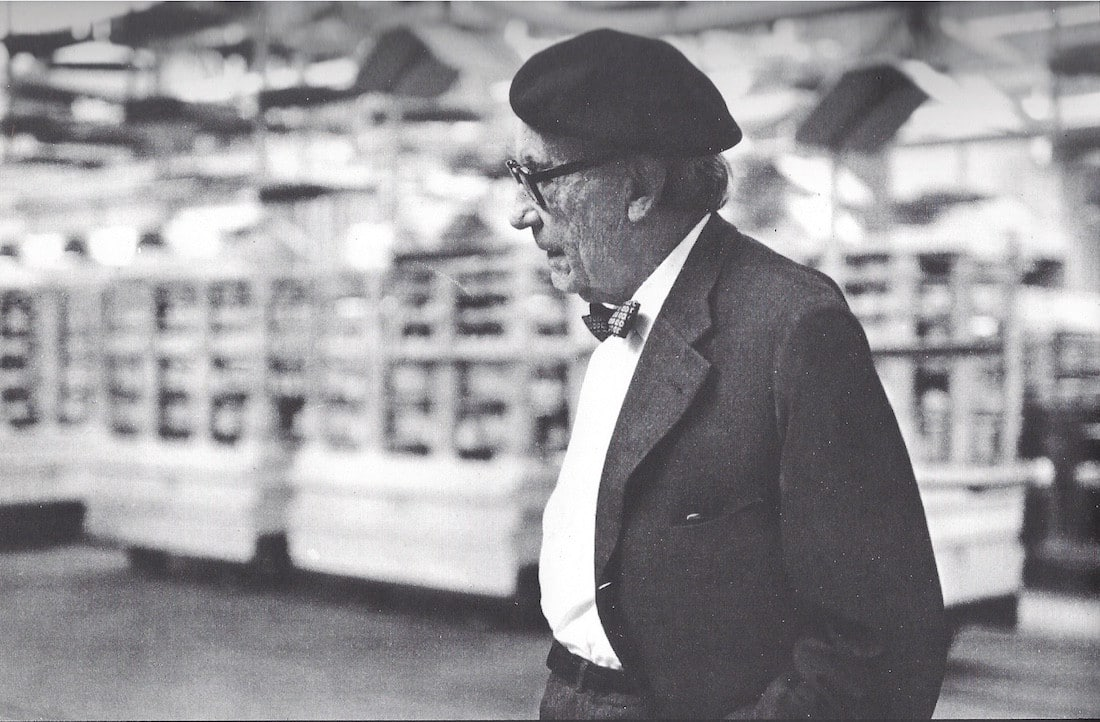 Walter Gropius mit dunkler Baskenmütze in einer Produktionsumgebung; historische Schwarzweißaufnahme.