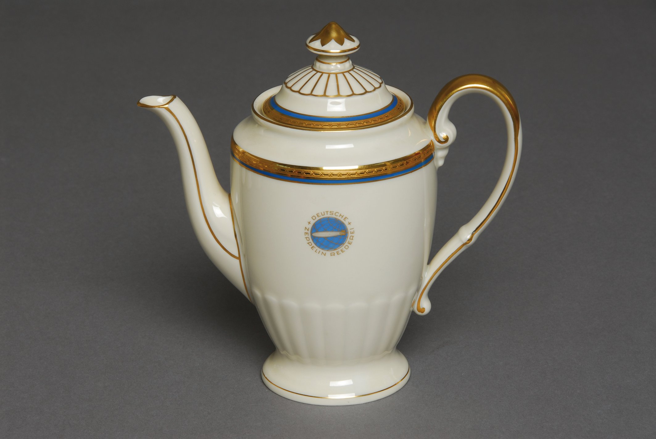 Elfenbeinfarbene Heinrich-Kaffeekanne mit blau-goldenen Bändern und rundem Zeppelin-Emblem.