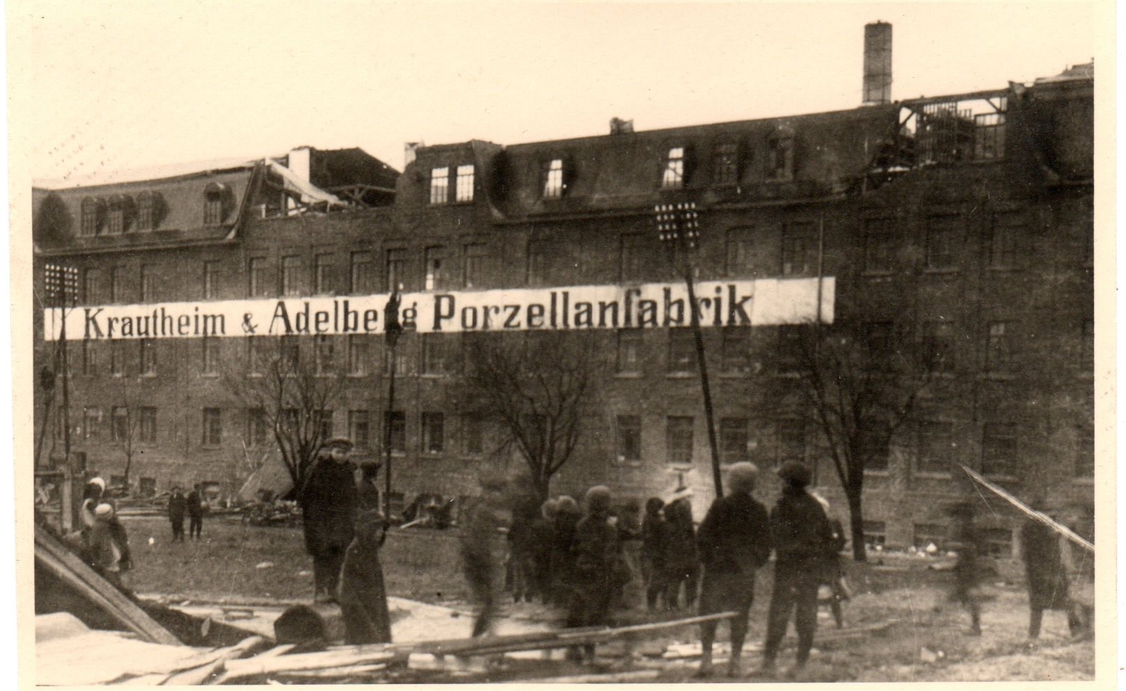 Brandaufnahme der Fabrik Krautheim und Adelberg mit beschädigtem Dach, Menschen und Schläuchen im Vordergrund.