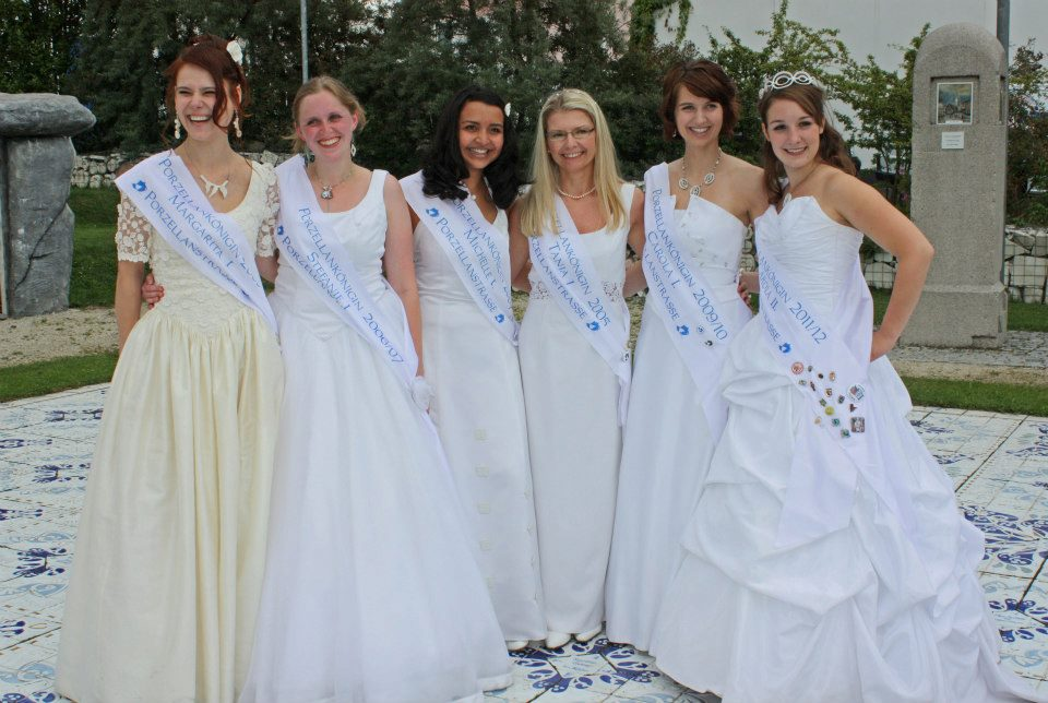 Gruppenaufnahme von sechs Frauen mit festlichen Kleidern und Schärpen der Porzellanstraße, auf denen unterschiedliche Amtsjahre stehen.