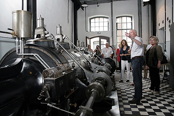 Besuchergruppe mit Mitarbeiter an der historischen Dampfmaschine.