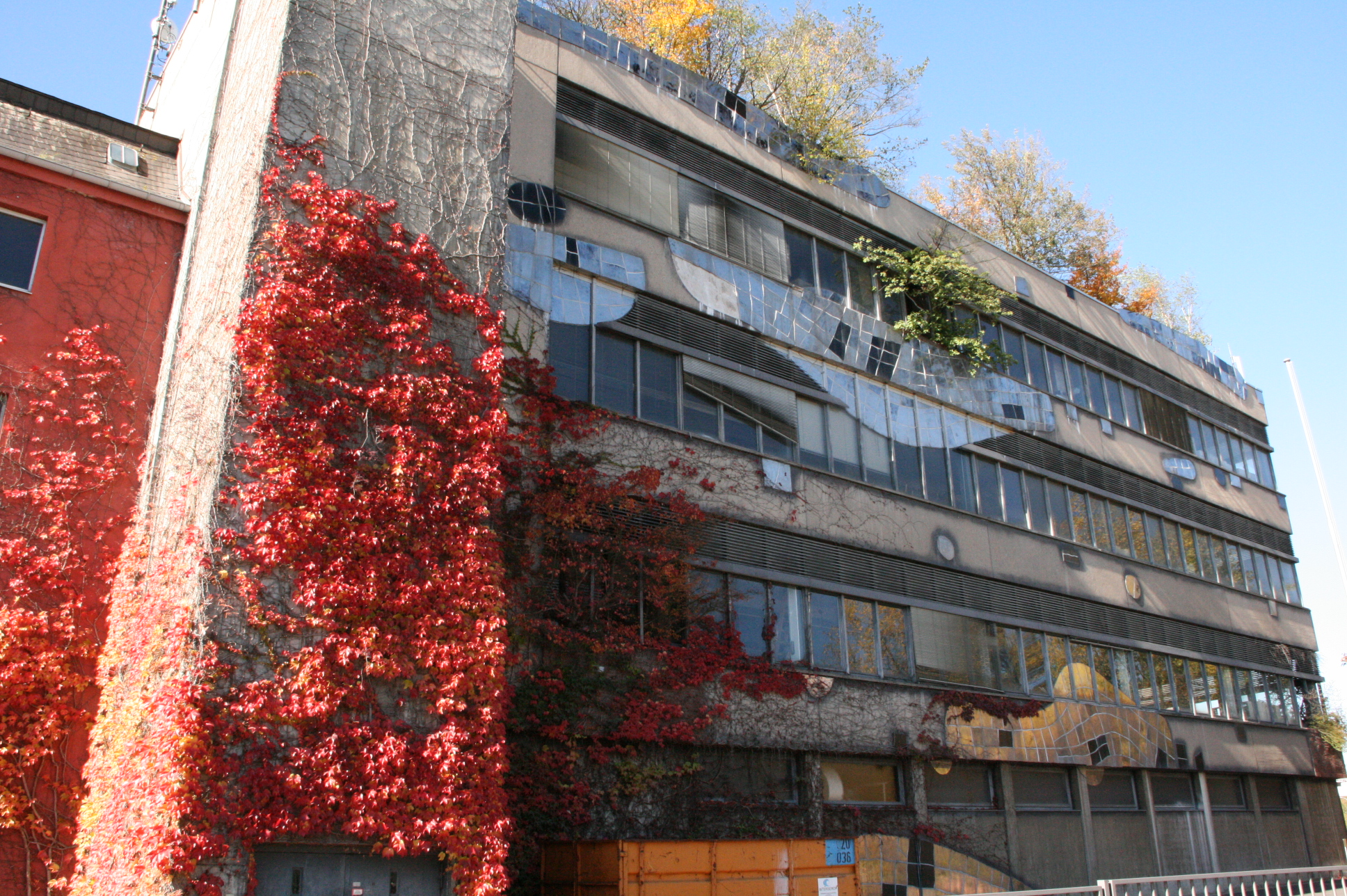 Hundertwassers Rosenthal-Fassade mit wellenförmigen Keramikbändern, Kletterpflanzen und Bäumen auf dem Dach.