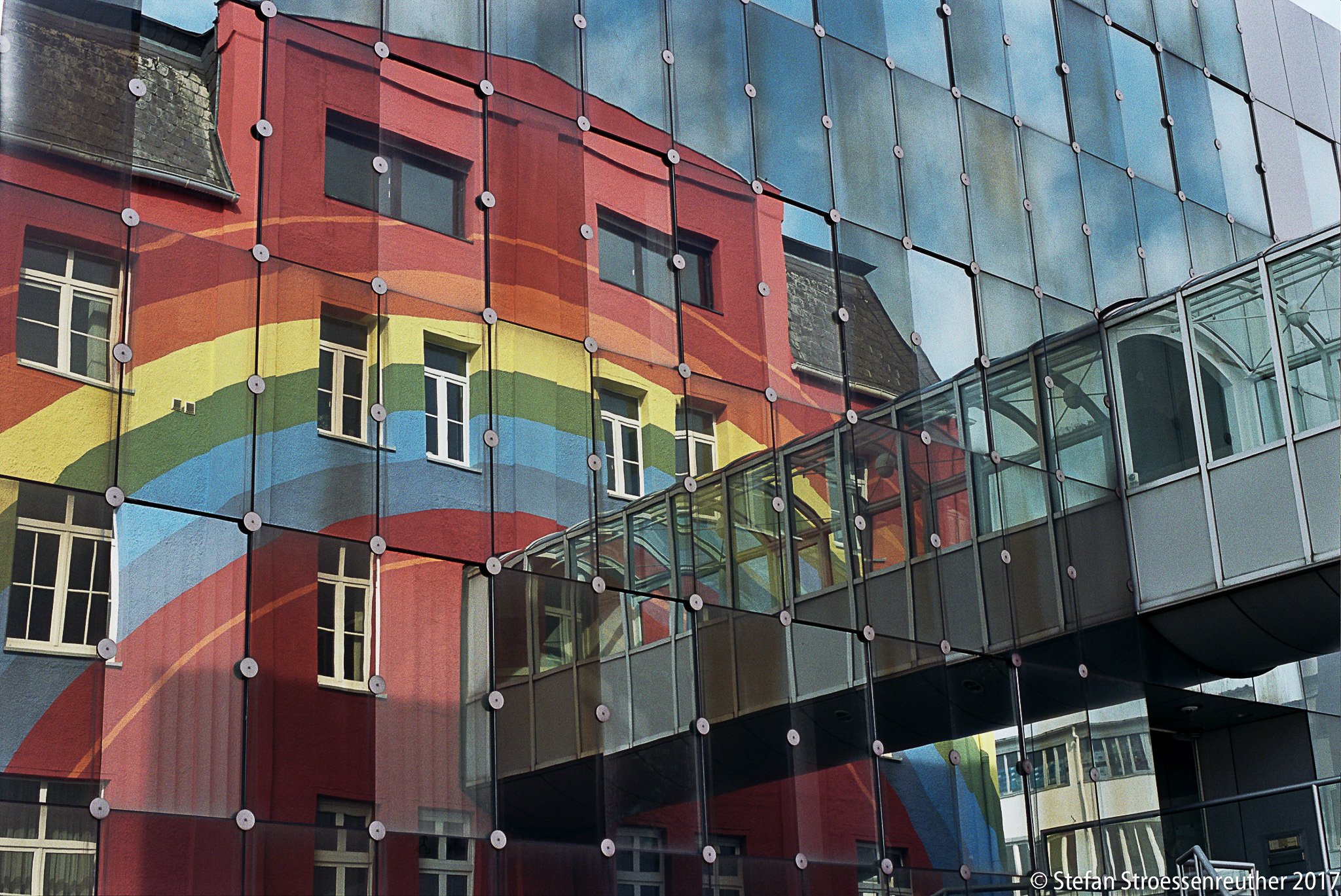 Morandinis geometrische Spiegelfassade mit dem gespiegelten Regenbogenhaus und einem verglasten Verbindungssteg.