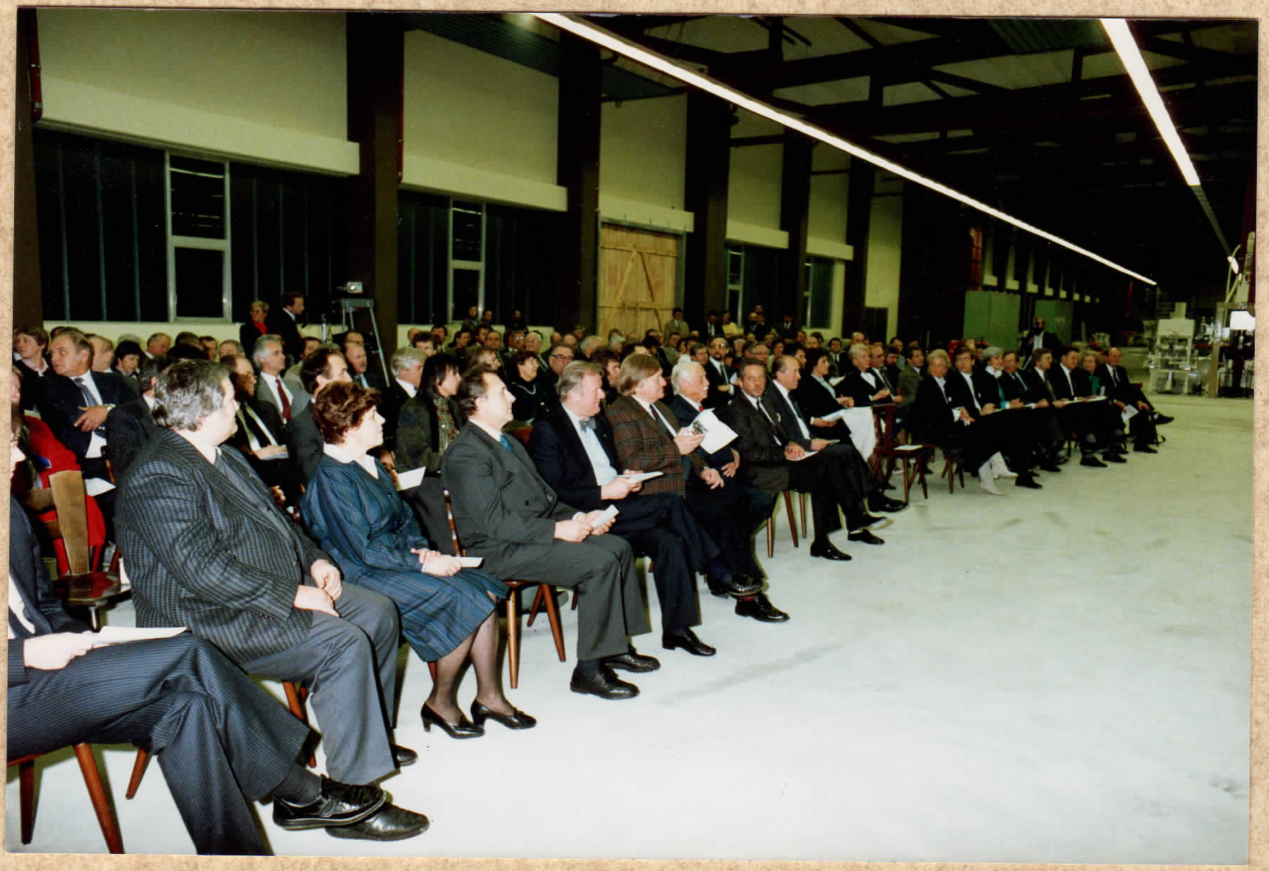 Gäste sitzen in mehreren Stuhlreihen in einer Werkhalle bei der Veranstaltung von 1987.