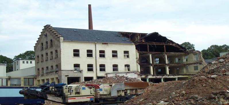 Teilweise abgebrochenes Fabrikgebäude am Standort Ludwigsmühle mit Abbruchmaschinen und erhaltenem Schornstein.