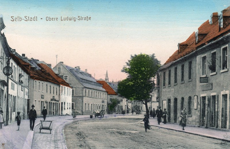 Historisch kolorierte Postkarte mit der gedruckten Aufschrift Selb-Stadt, Obere Ludwig-Straße, mit Häuserzeilen und einem Fuhrwerk.