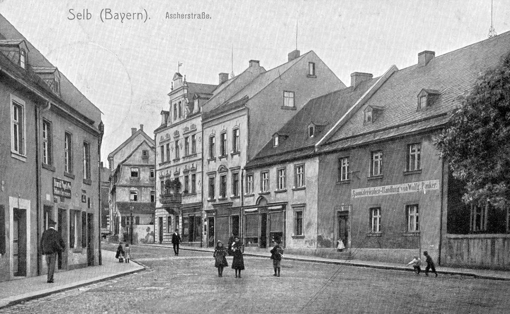 Historische Schwarzweißpostkarte mit der gedruckten Aufschrift Selb Bayern Ascherstraße, Häuserzeilen und Menschen auf der gepflasterten Straße.