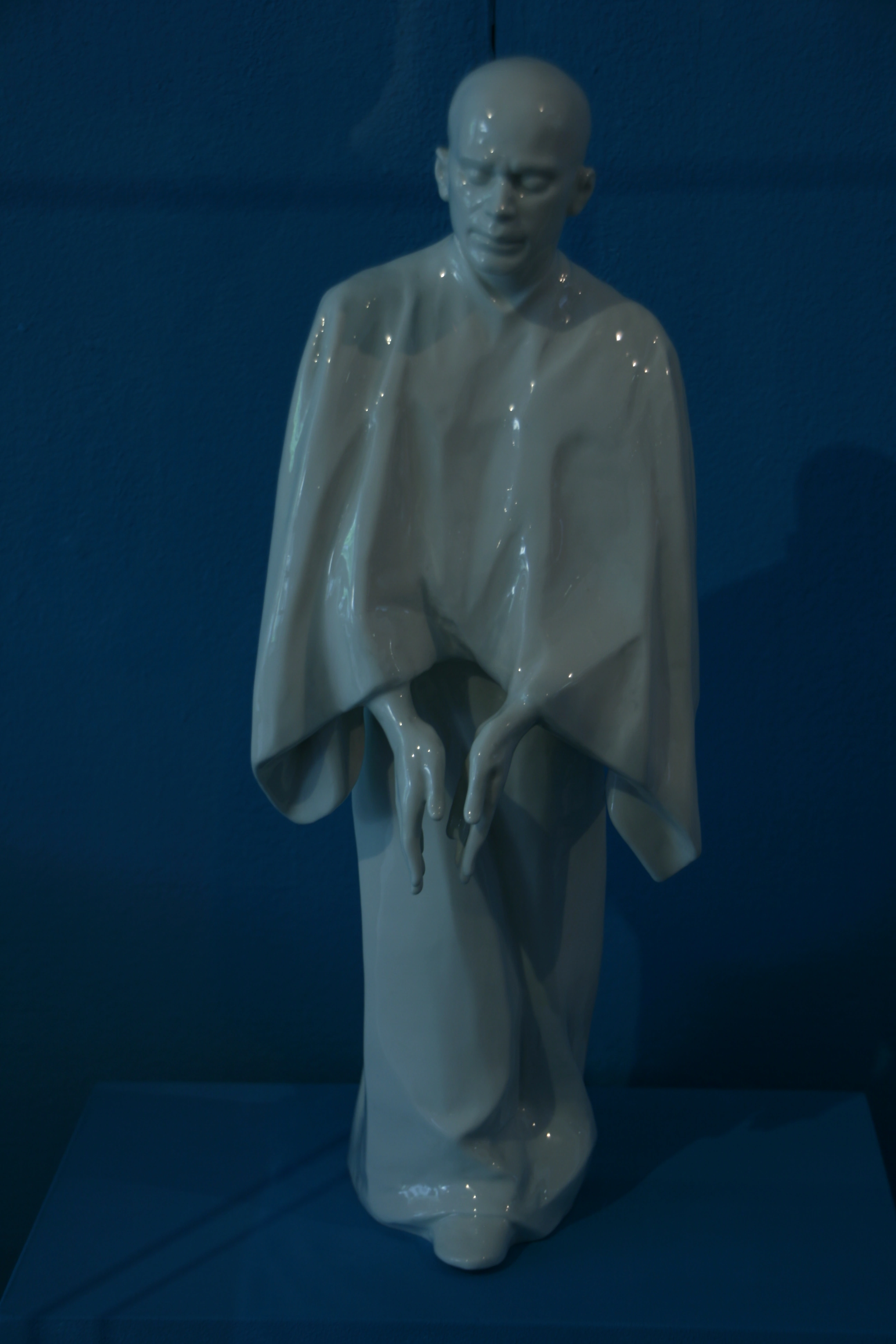 Weiße stehende Tanzfigur mit gesenktem Blick und vor den Körper geführten Händen.