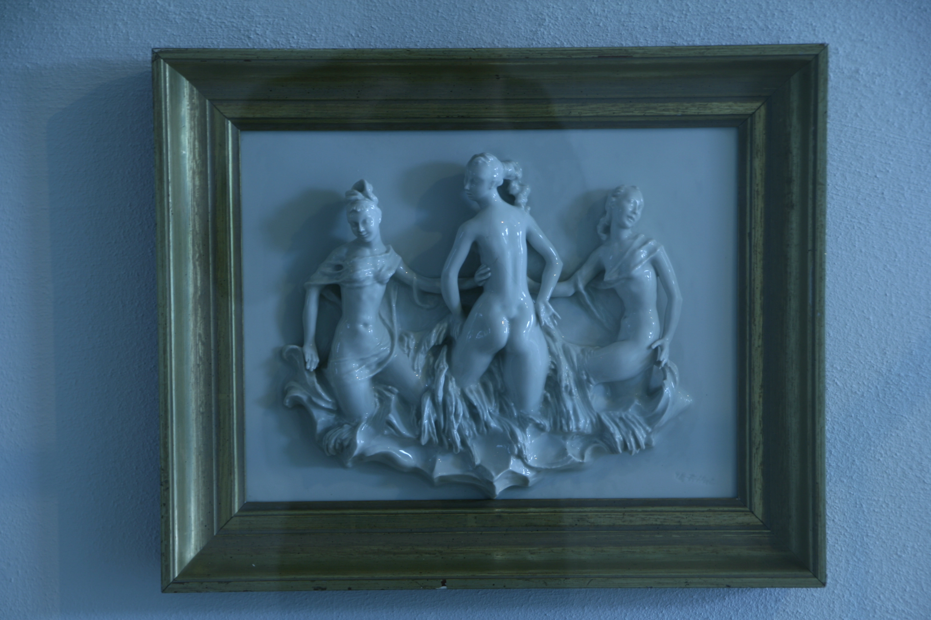 Gerahmtes weißes Relief mit drei Frauenfiguren und bewegtem Tuch beziehungsweise Gewand.
