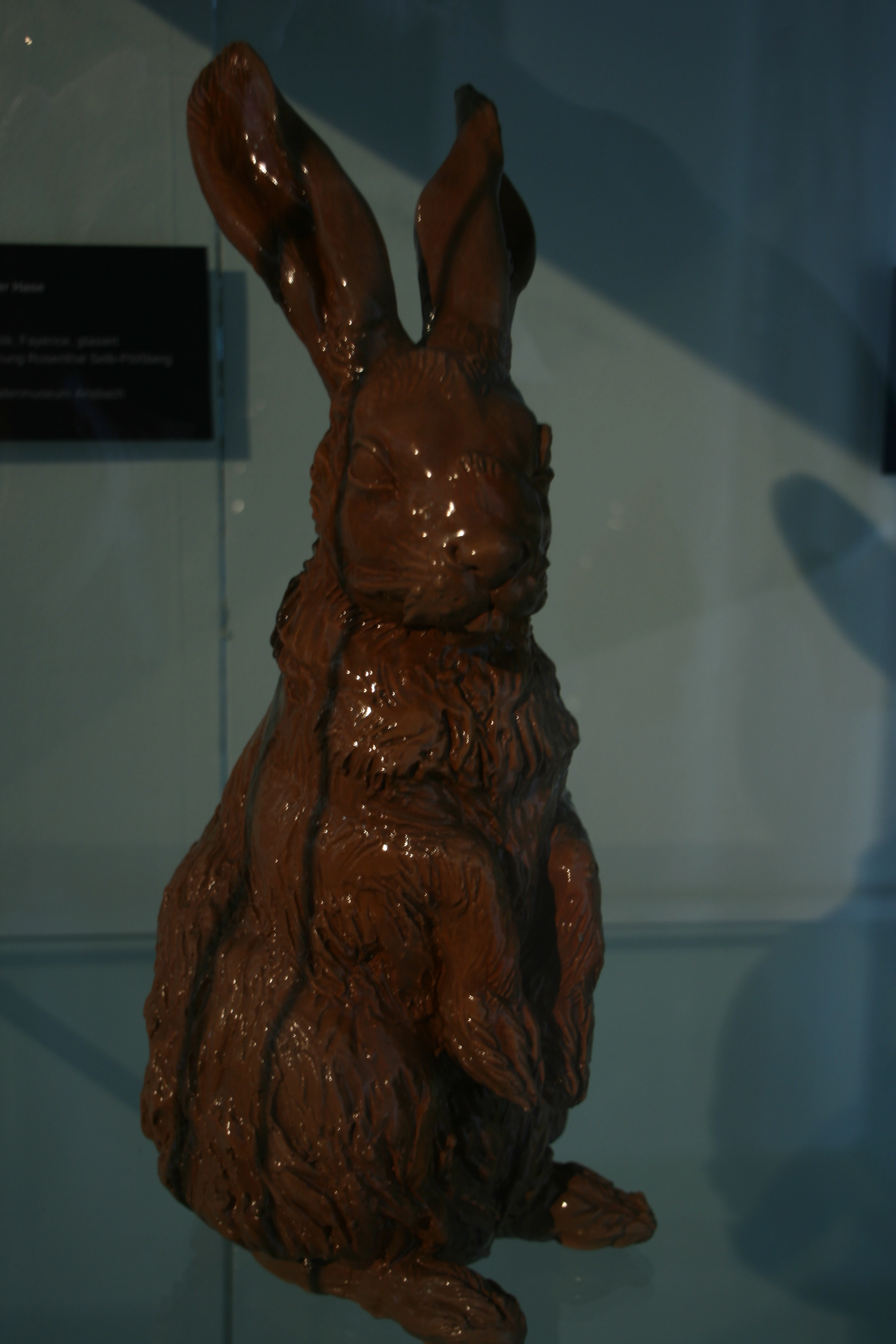 Braun glasierte sitzende Hasenfigur mit langen aufgerichteten Ohren in einer Museumsvitrine.