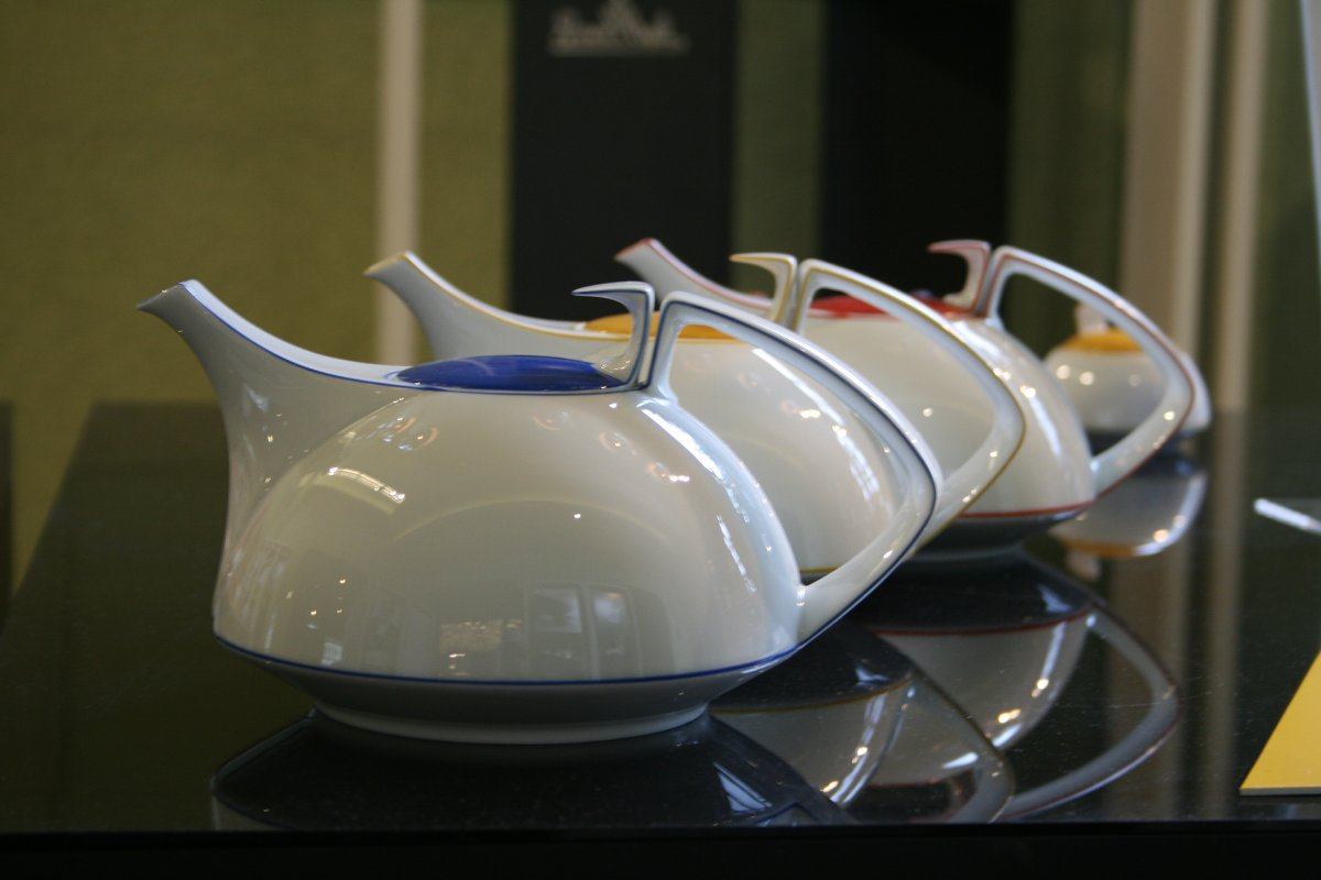 Mehrere helle Kannen mit farbigen Rändern auf einer dunklen Ausstellungsfläche, 2009.