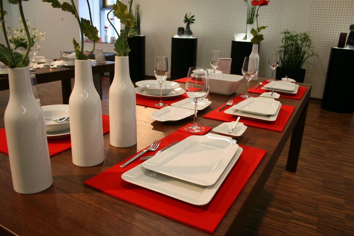 Mit weißem Geschirr, Gläsern und hohen Vasen gedeckter Tisch auf roten Platzunterlagen, 2009.