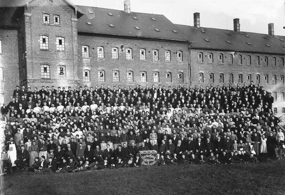 Große Belegschaft der Porzellanfabrik vor einem mehrgeschossigen Fabrikgebäude mit vielen Fenstern.