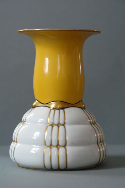 Vase mit gelbem, ausgestelltem Hals und weißem, plastisch gegliedertem Unterteil sowie goldfarbenen Akzenten.