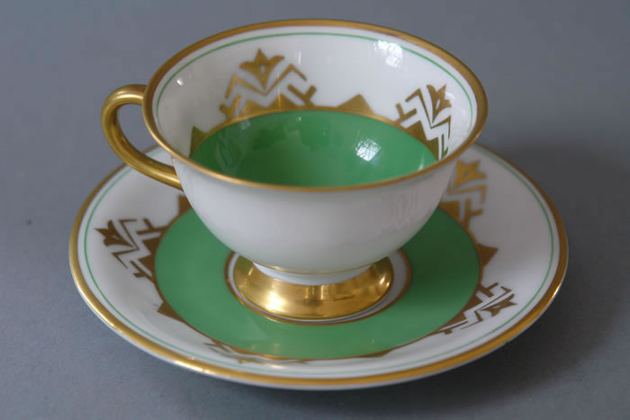 Tasse mit grünem Inneren, goldfarbenem Fuß und Henkel sowie passender Untertasse mit grünem und goldenem Dekor.