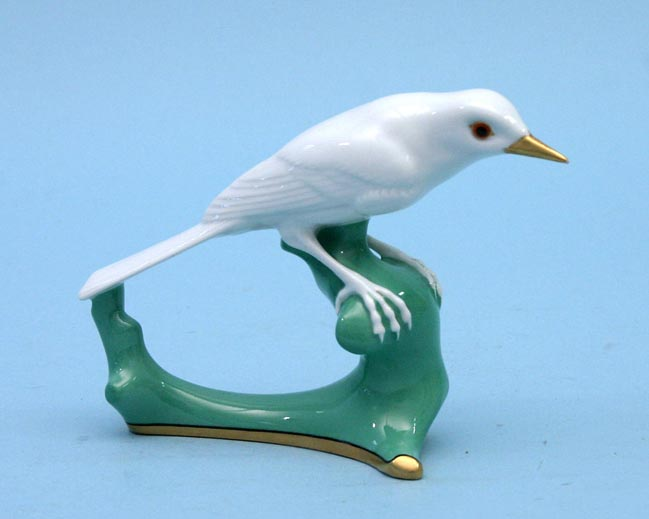 Weiße Bachstelzenfigur mit gelbem Schnabel auf einem grünen, bogenförmigen Astsockel.